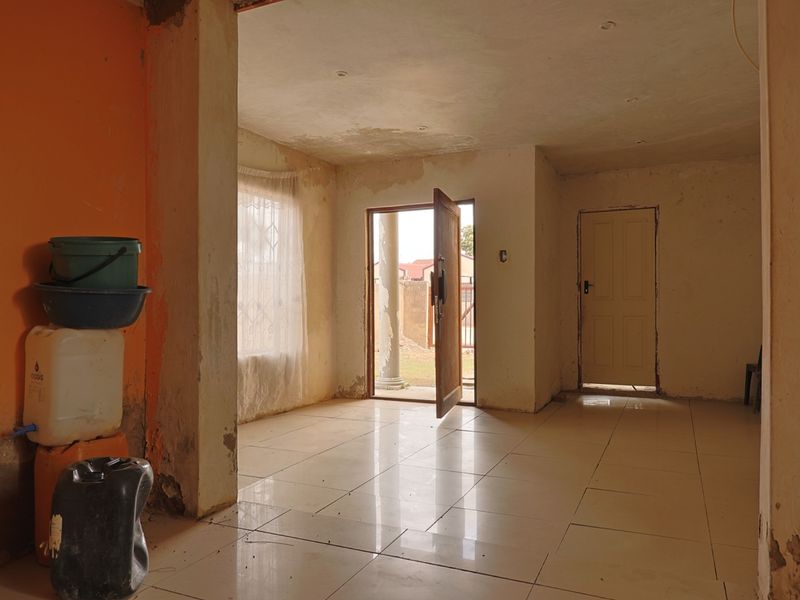 An empty living area featuring tiled flooring and recessed lighting, currently requiring cosmetic renovation and wall repairs to restore its condition.