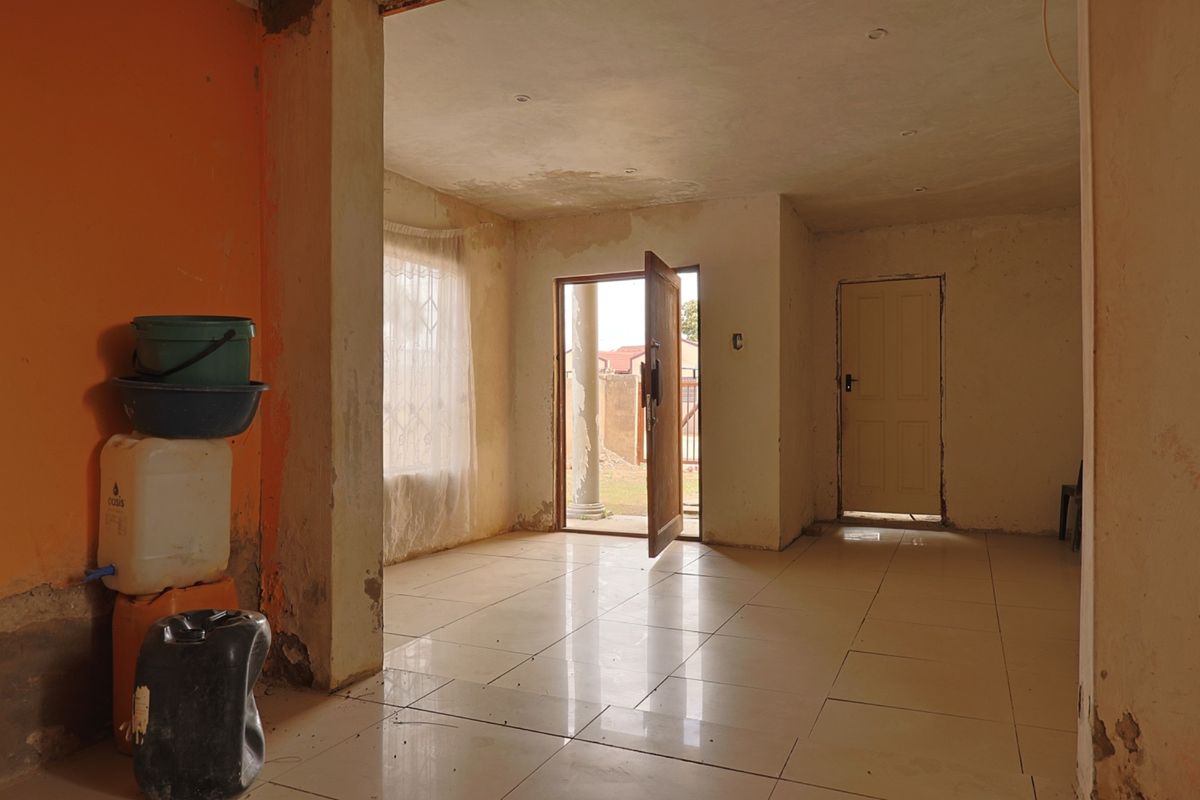 An empty living area featuring tiled flooring and recessed lighting, currently requiring cosmetic renovation and wall repairs to restore its condition.