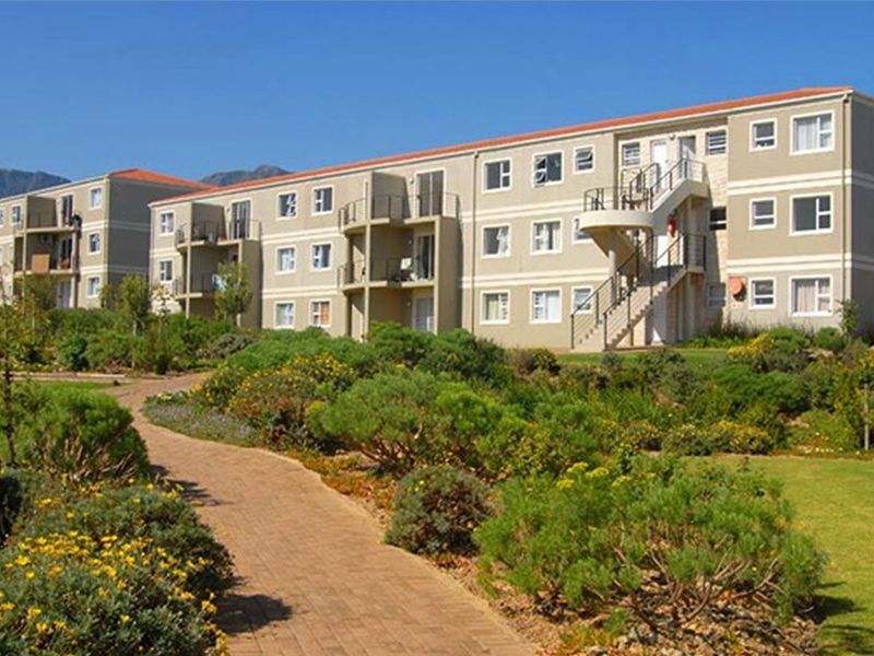 A view of the apartment complex exterior featuring landscaped gardens, paved walkways, and multi-level balconies with external staircases.