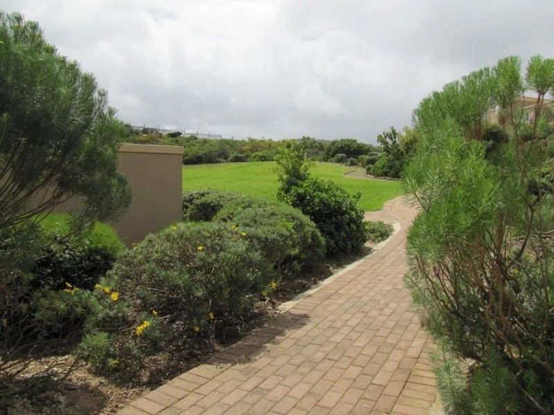 A well-maintained garden area featuring a paved brick walkway leading through landscaped greenery and open lawn space.