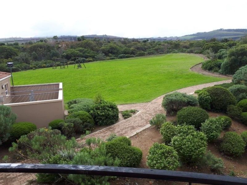A well-maintained garden area featuring a paved walkway, expansive lawn, and established shrubbery, viewed from an elevated position.