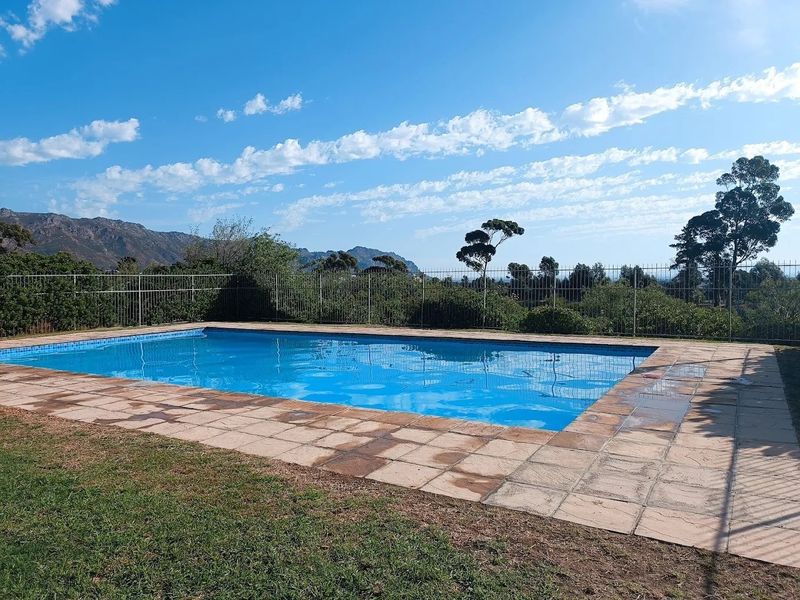 Outdoor swimming pool area featuring a paved surround, metal perimeter fencing, and scenic mountain views.