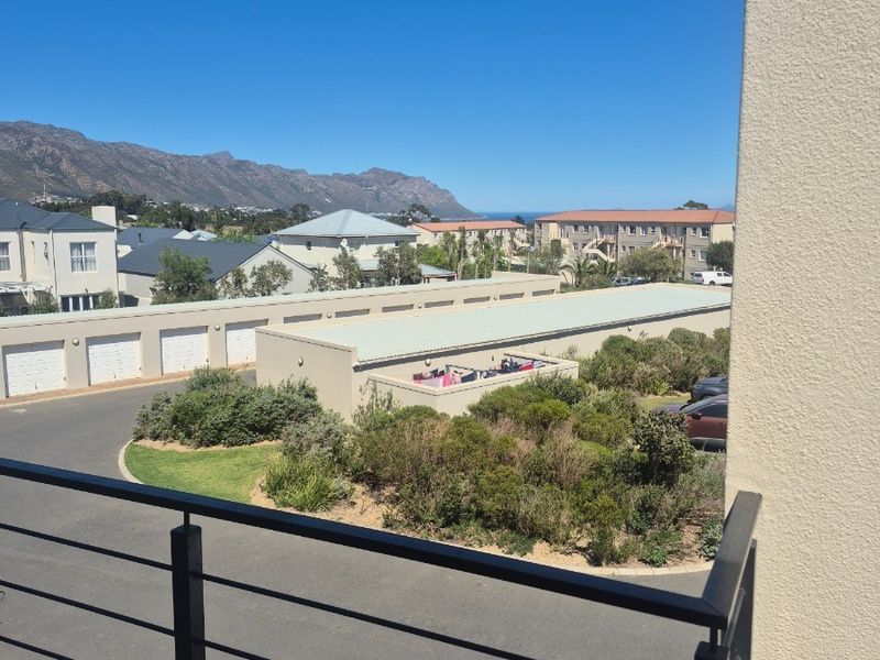 An elevated view from a balcony overlooking the apartment complex grounds, parking area, and surrounding mountain landscape.