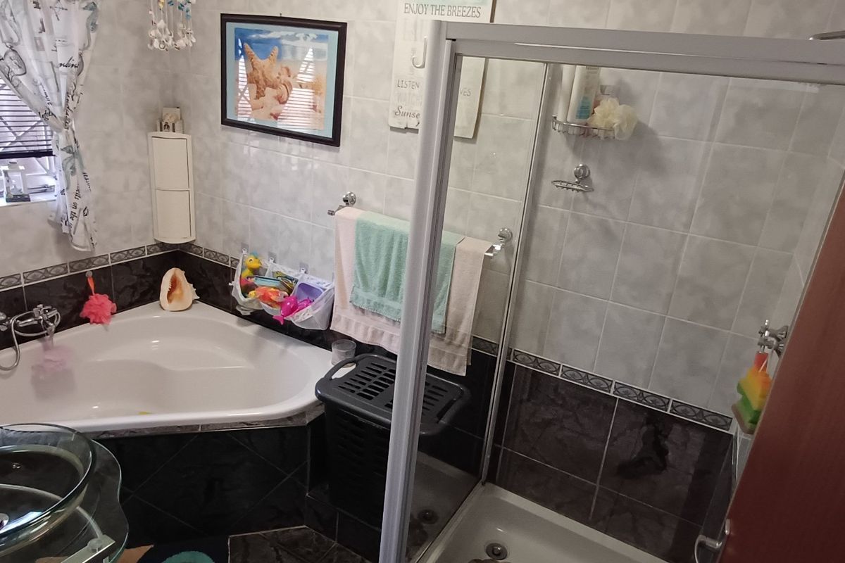 A functional bathroom featuring a corner bathtub, a separate glass-enclosed shower, and tiled walls, offering a practical layout for daily use.