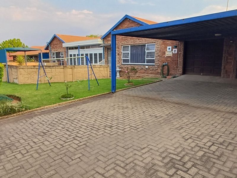 Front view of the property featuring a paved driveway, a covered carport, a brick facade, and a small front garden area.