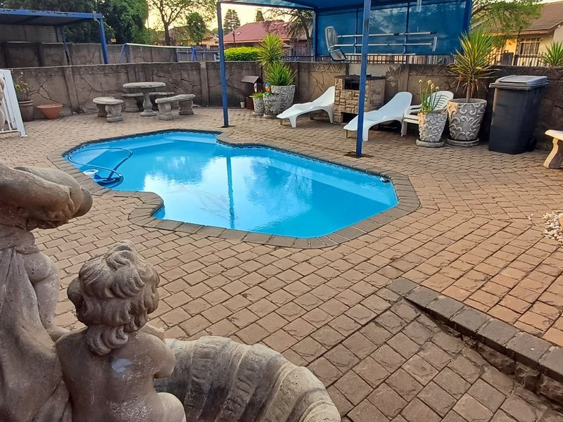 Outdoor pool area featuring a paved patio, built-in braai, and a decorative water feature, enclosed by a boundary wall.