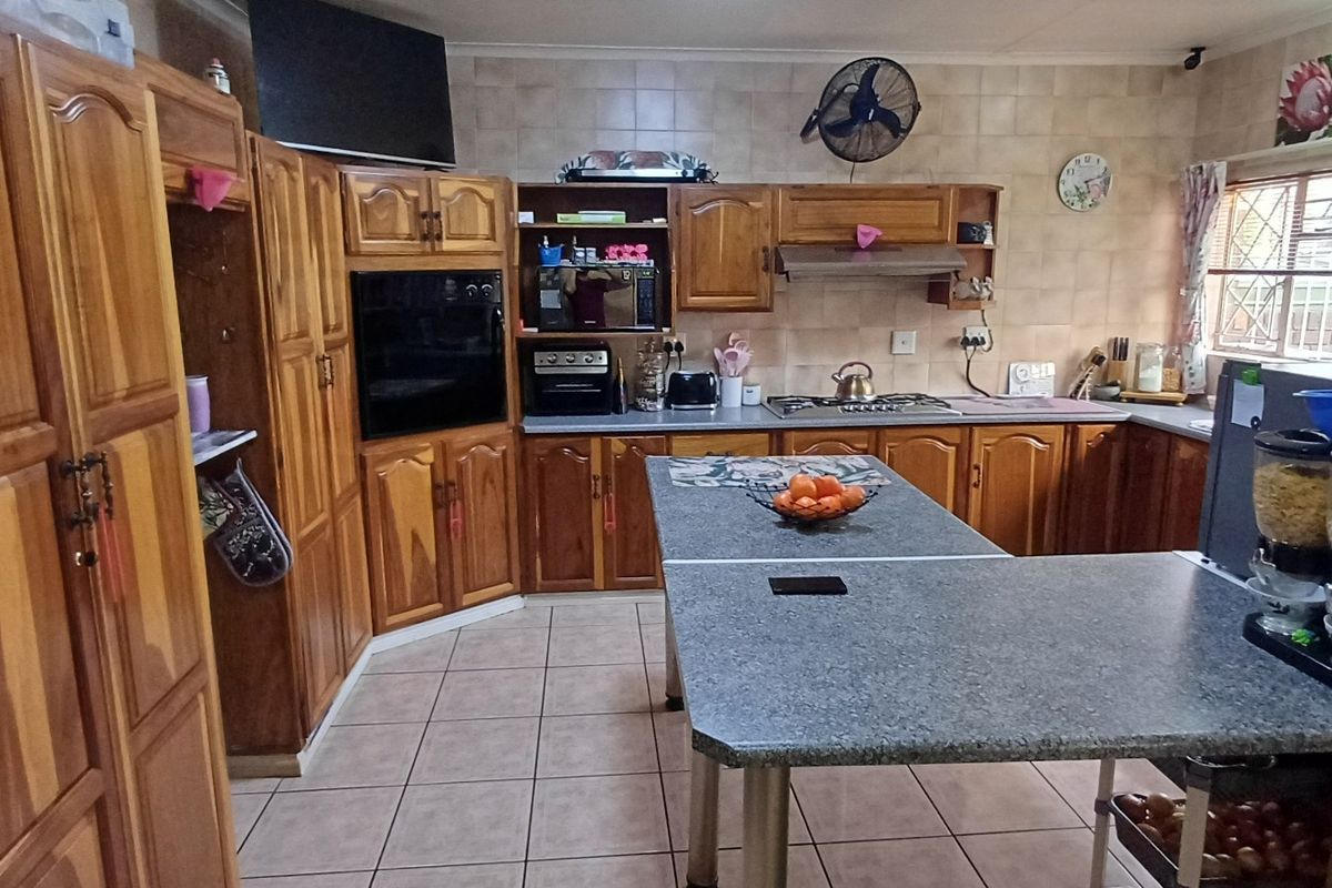A functional kitchen featuring extensive wooden cabinetry, a central island, built-in oven, gas hob, and tiled finishes throughout.