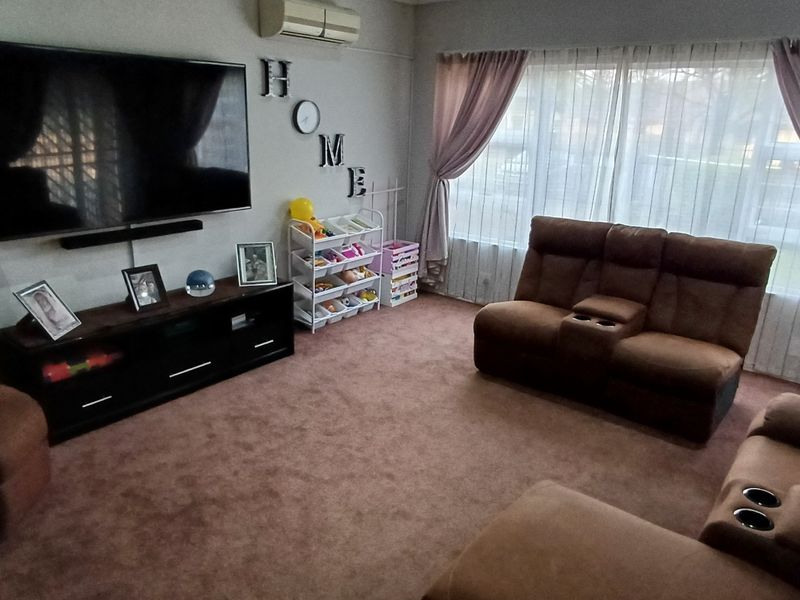 A comfortable living room featuring wall-mounted air conditioning, large windows with curtains, and a gas heater for climate control.