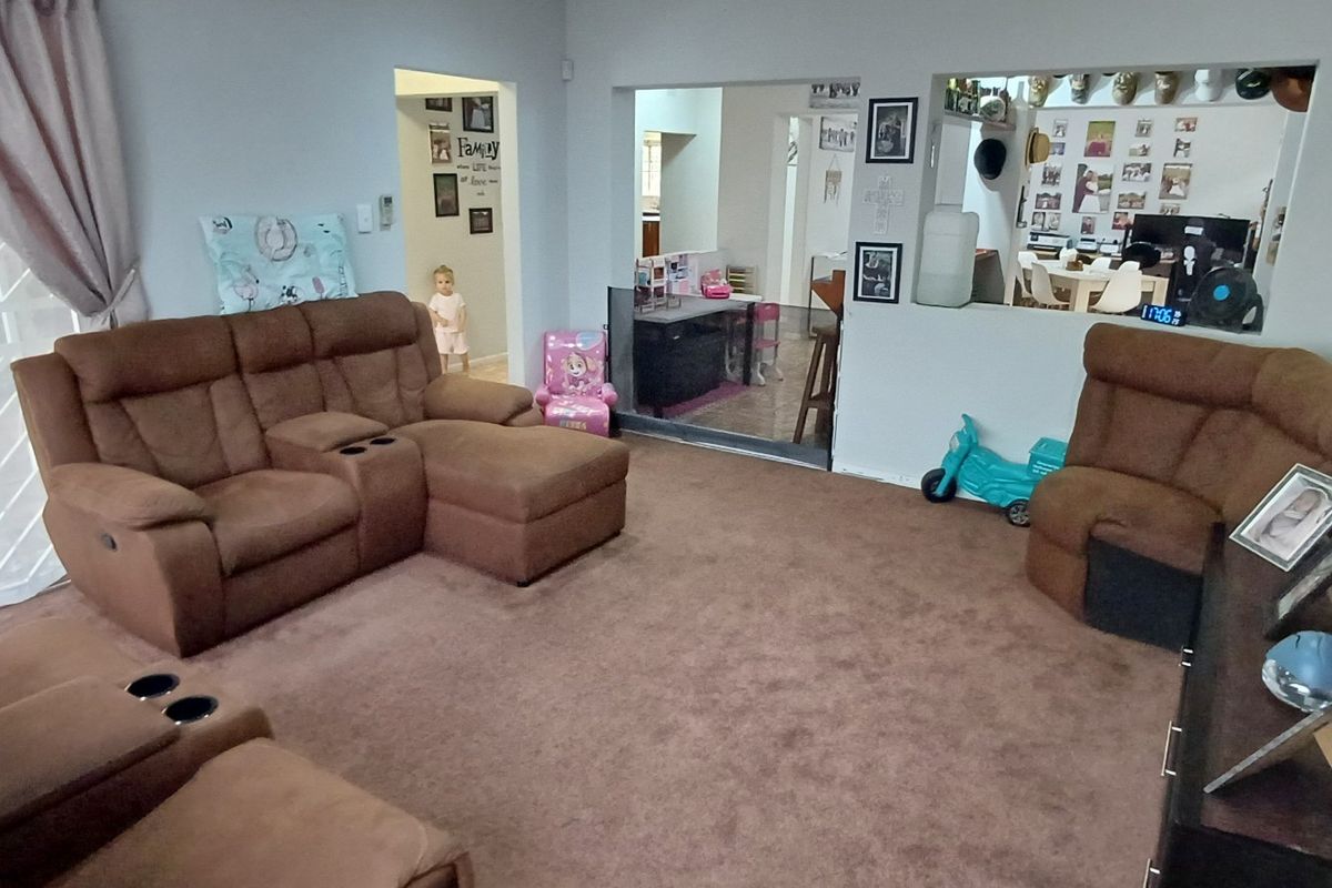 A spacious living room featuring carpeted flooring, a sliding glass door with security gate, and a convenient pass-through window connecting to the adjacent area.