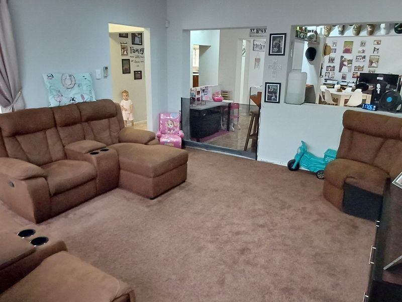 A spacious living room featuring carpeted flooring, a sliding glass door with security gate, and a convenient pass-through window connecting to the adjacent area.