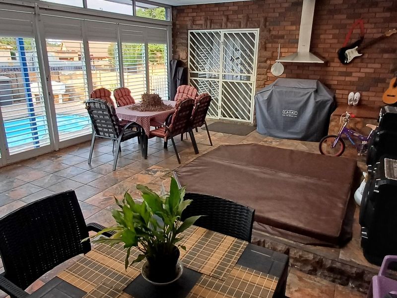 Spacious enclosed patio area featuring tiled flooring, exposed brick walls, and a built-in braai, offering direct access to the pool area.