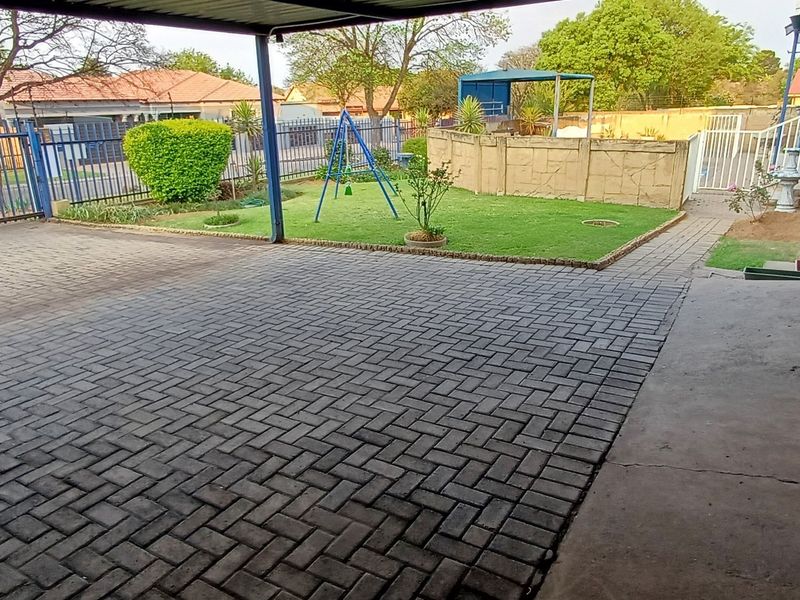 A paved front driveway and carport area featuring a small lawn, perimeter fencing, and stone-clad exterior walling.