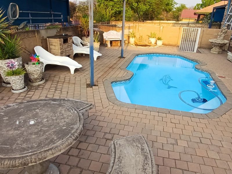 Outdoor pool area featuring a paved patio, built-in braai, and a swimming pool with boundary walling.