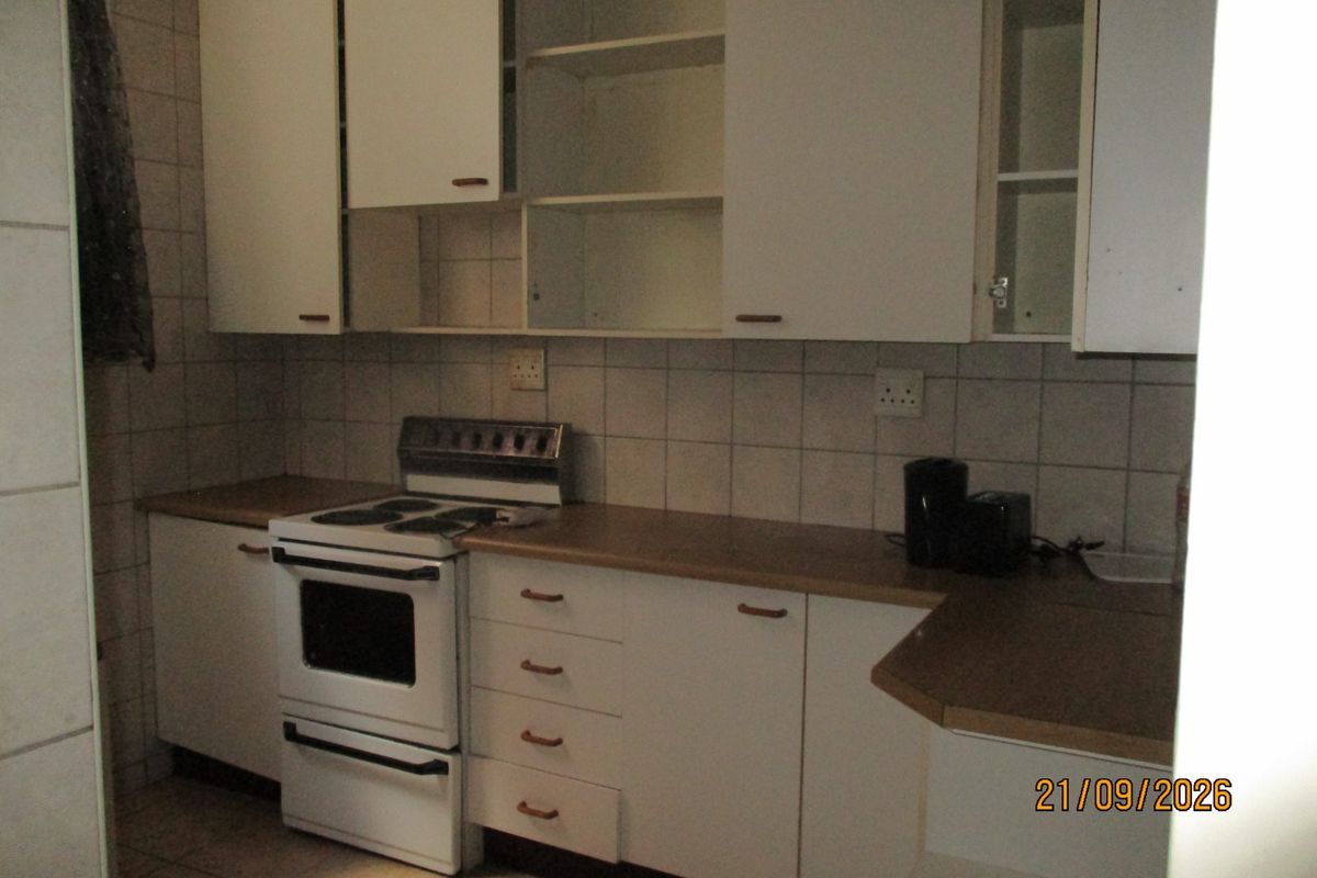 A dated kitchen featuring white cabinetry, laminate countertops, and a tiled backsplash, requiring cosmetic updates to modernize the space.