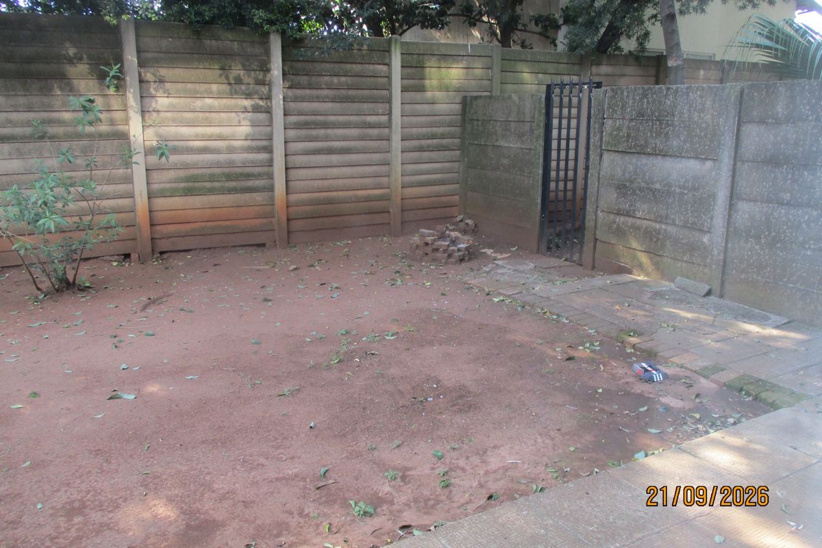 A private rear courtyard area featuring a precast concrete boundary wall, a metal pedestrian gate, and a paved walkway section.