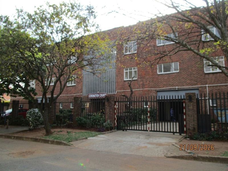 Front elevation of Coronation Court townhouse complex featuring a brick facade, secure gated entrance, and paved driveway access.