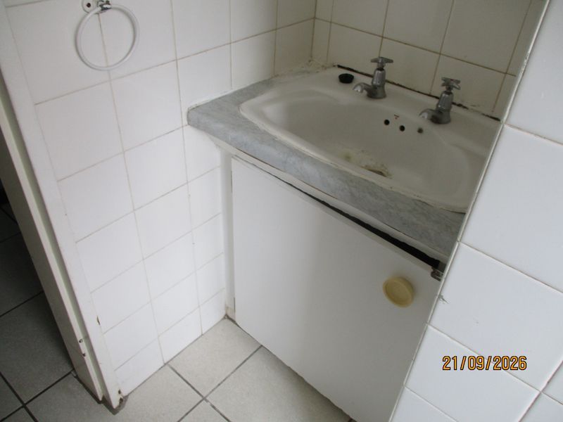 A dated bathroom vanity area featuring a built-in basin, tiled splashback, and storage cabinet, currently requiring maintenance and cosmetic updates.