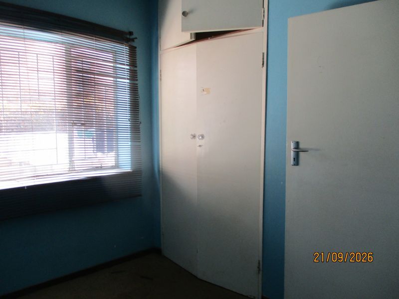 A vacant bedroom featuring a built-in wardrobe, venetian blinds, and blue painted walls, requiring cosmetic updates to improve its overall condition.