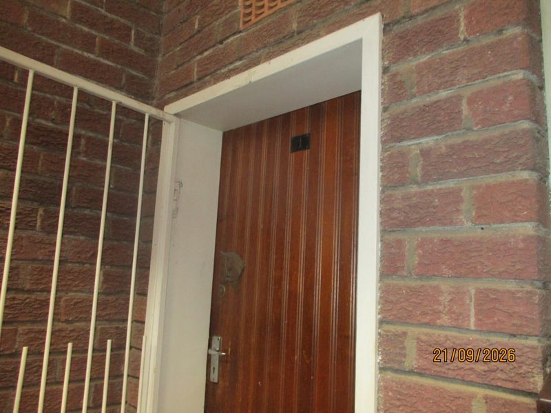 Exterior view of a townhouse entrance featuring a brick facade, a security gate, and a timber front door.