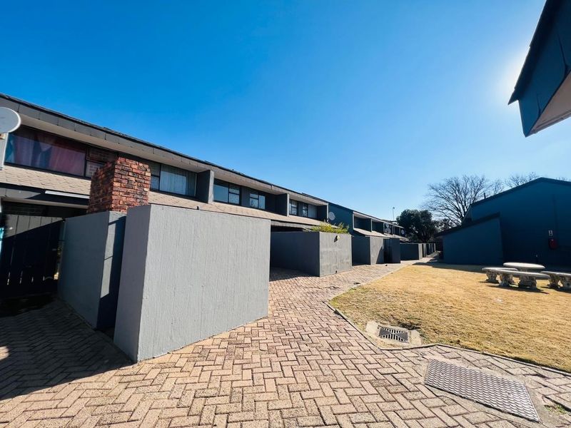 Rear exterior view of the townhouse complex featuring a paved walkway, brick chimney, and shared garden space.