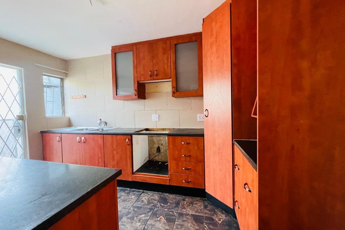 A dated kitchen featuring wood-look cabinetry, dark countertops, and tiled finishes, currently missing a stove and requiring cosmetic updates to modernize the space.