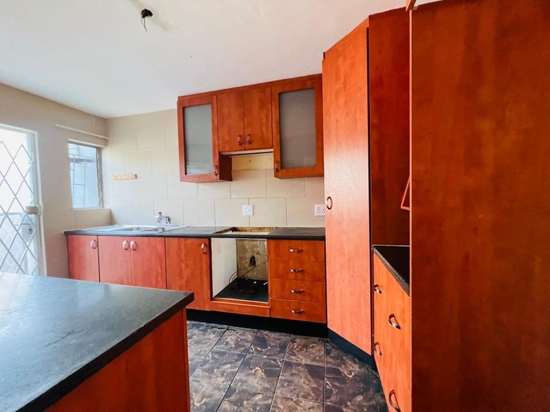 A dated kitchen featuring wood-look cabinetry, dark countertops, and tiled finishes, currently missing a stove and requiring cosmetic updates to modernize the space.