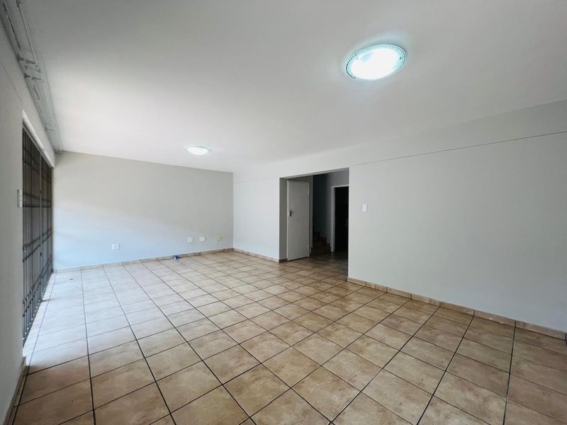 A spacious, empty living area featuring neutral walls, ceramic tile flooring, and flush mount ceiling lights, providing a blank canvas for interior design.