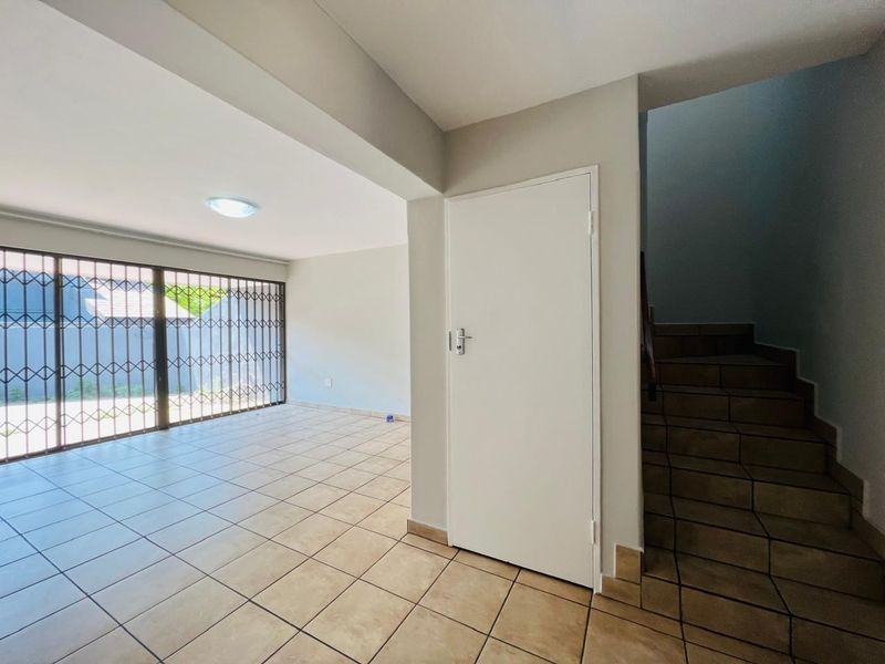 An open-plan living area featuring neutral tiled flooring, a security gate, and an adjacent staircase leading to the upper level.