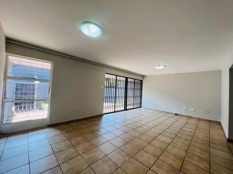 A spacious, empty living area featuring neutral ceramic floor tiles, security gates, and security bars on the windows, providing a blank canvas for personalization.
