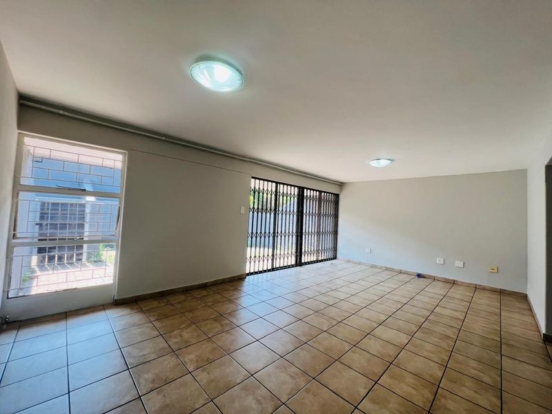 A spacious, empty living area featuring neutral tiled flooring, security gates, and large windows with security bars, offering a blank canvas for personalization.