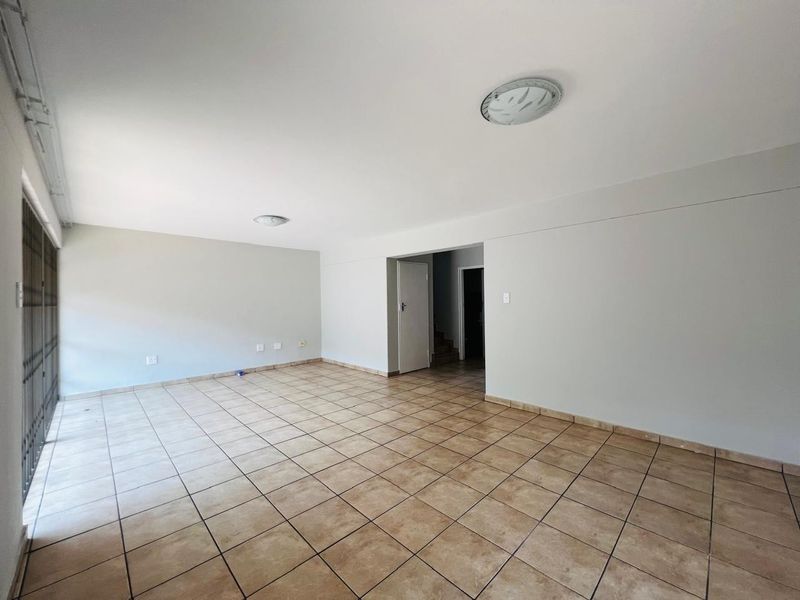 A spacious, empty living area featuring neutral walls, tiled flooring, and direct access to a secure patio area.