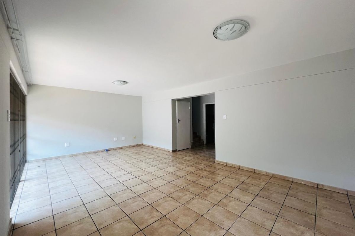 A spacious, empty living area featuring neutral walls, tiled flooring, and direct access to a secure patio area.