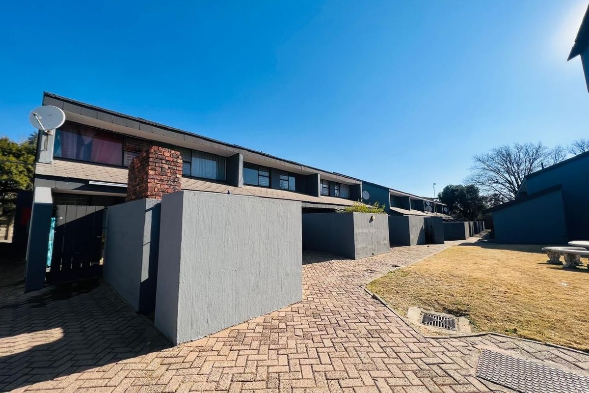 Rear view of a townhouse complex featuring paved walkways, private boundary walls, and brick chimneys under a clear blue sky.