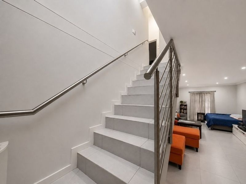 A modern staircase featuring tiled steps and a sleek stainless steel handrail, leading to an open-plan living area with neutral finishes.