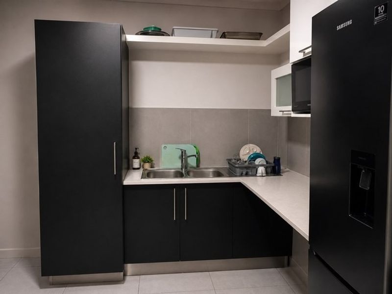 A modern scullery featuring dark cabinetry, stone countertops, a double bowl sink, and integrated microwave, providing efficient additional prep and wash-up space.