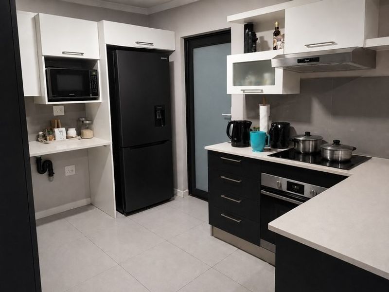 Modern kitchen featuring sleek black and white cabinetry, stone countertops, integrated appliances, and tiled flooring with direct access to an exterior door.