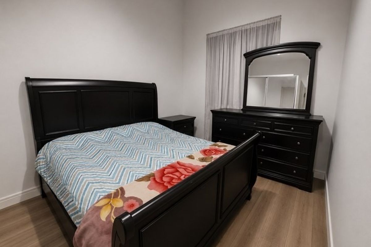 A well-maintained bedroom featuring light-toned laminate flooring, neutral walls, and a built-in wardrobe with sliding doors.