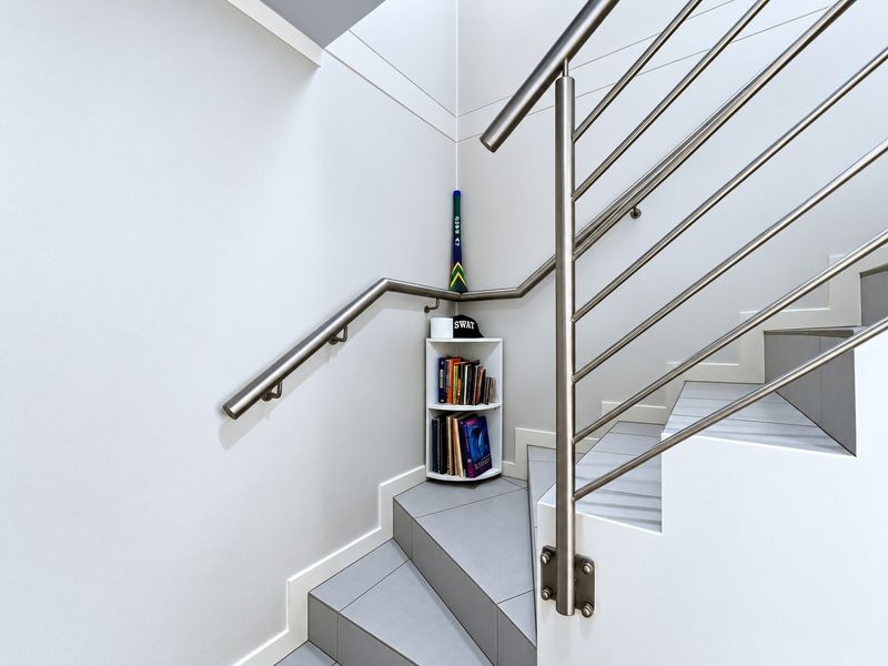A modern staircase featuring clean white walls, grey tiled steps, and a contemporary stainless steel balustrade.