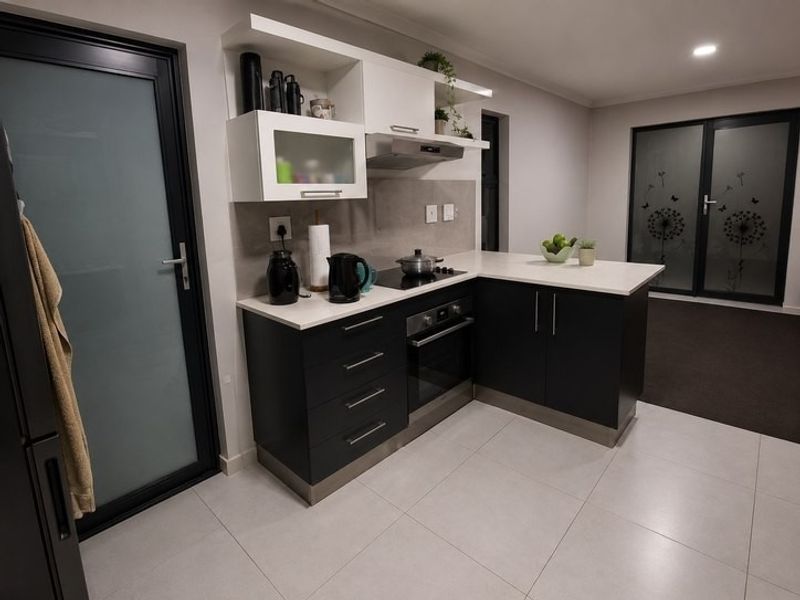 Modern kitchen featuring dark cabinetry, stone countertops, integrated oven and hob, and tiled flooring with direct access to outdoor areas.