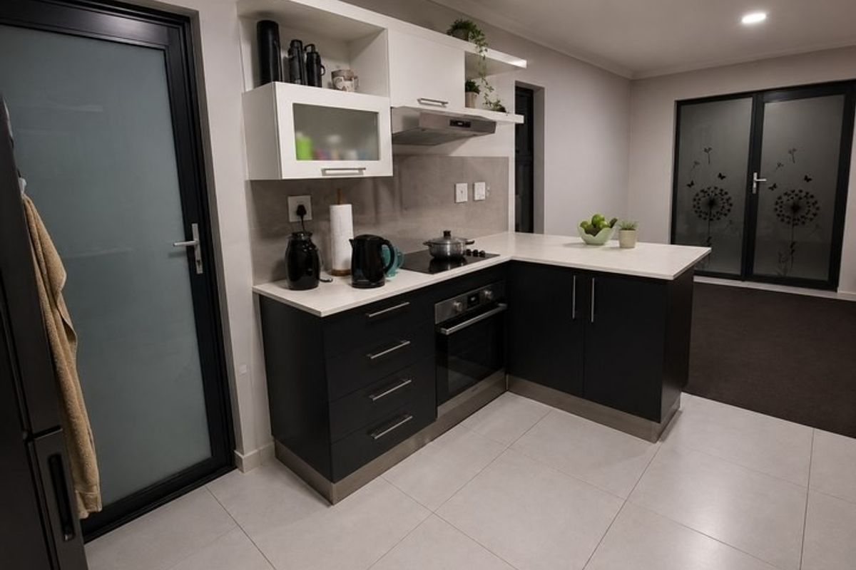 Modern kitchen featuring dark cabinetry, stone countertops, integrated oven and hob, and tiled flooring with direct access to outdoor areas.