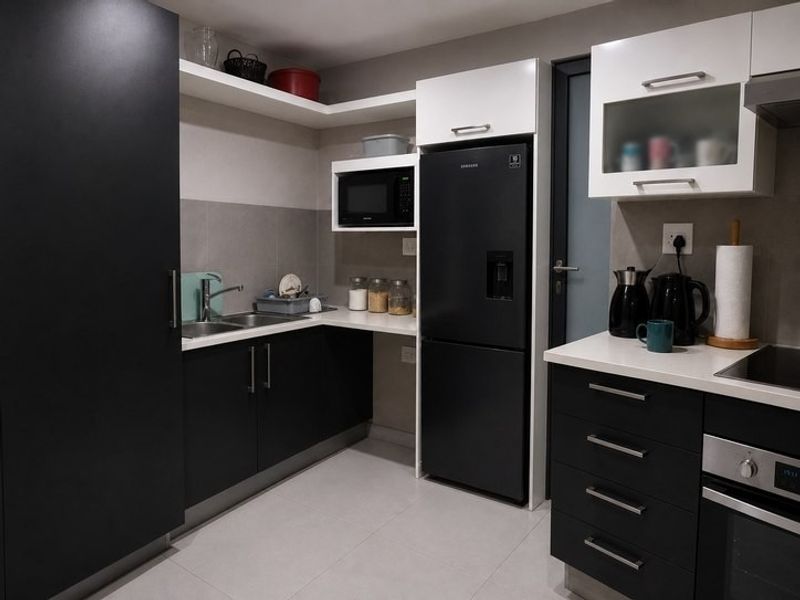 Modern kitchen featuring sleek black and white cabinetry, stone countertops, integrated appliances, and tiled flooring, offering a clean and functional workspace.