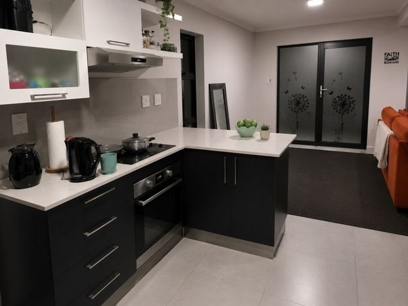 Modern open-plan kitchen featuring dark cabinetry, stone countertops, integrated appliances, and direct access to the living area through glass doors.