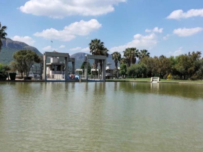 A scenic view of a lake featuring concrete structures and mature trees in the background under a clear blue sky.