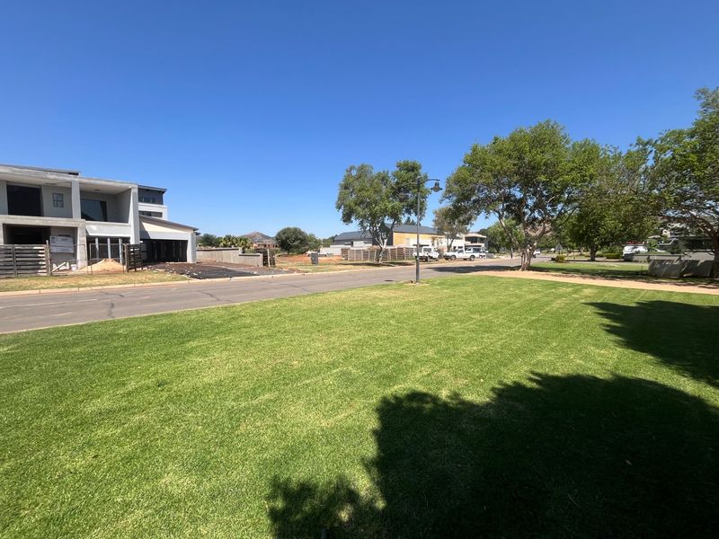 A clear street view of a residential area featuring a well-maintained lawn, mature trees, and paved road infrastructure in a quiet neighborhood setting.