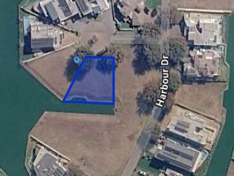 Aerial view of a vacant residential plot situated along a canal, offering direct waterfront access in a developed estate.