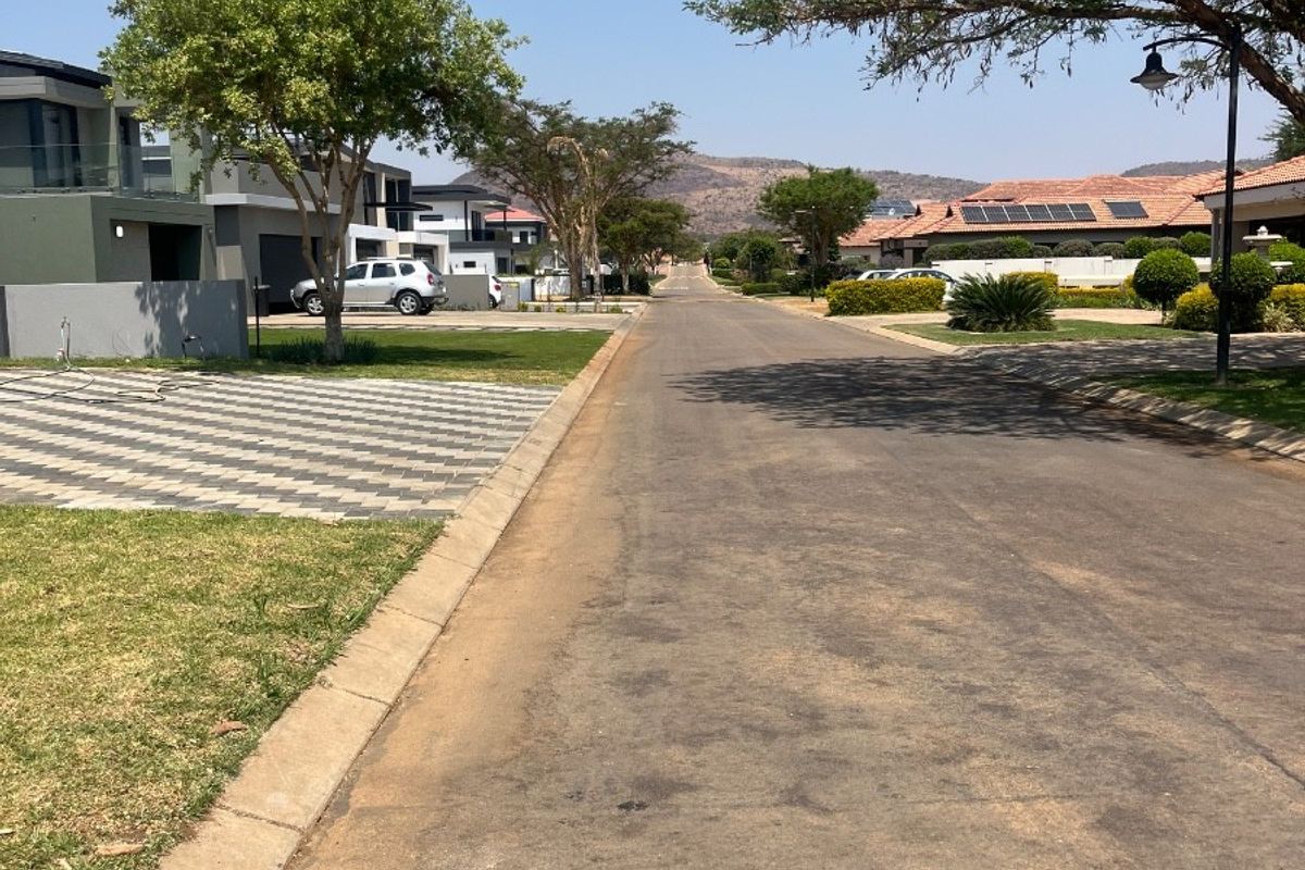 A clear street view of a well-maintained residential estate road with paved surfaces, concrete curbing, and established landscaping.