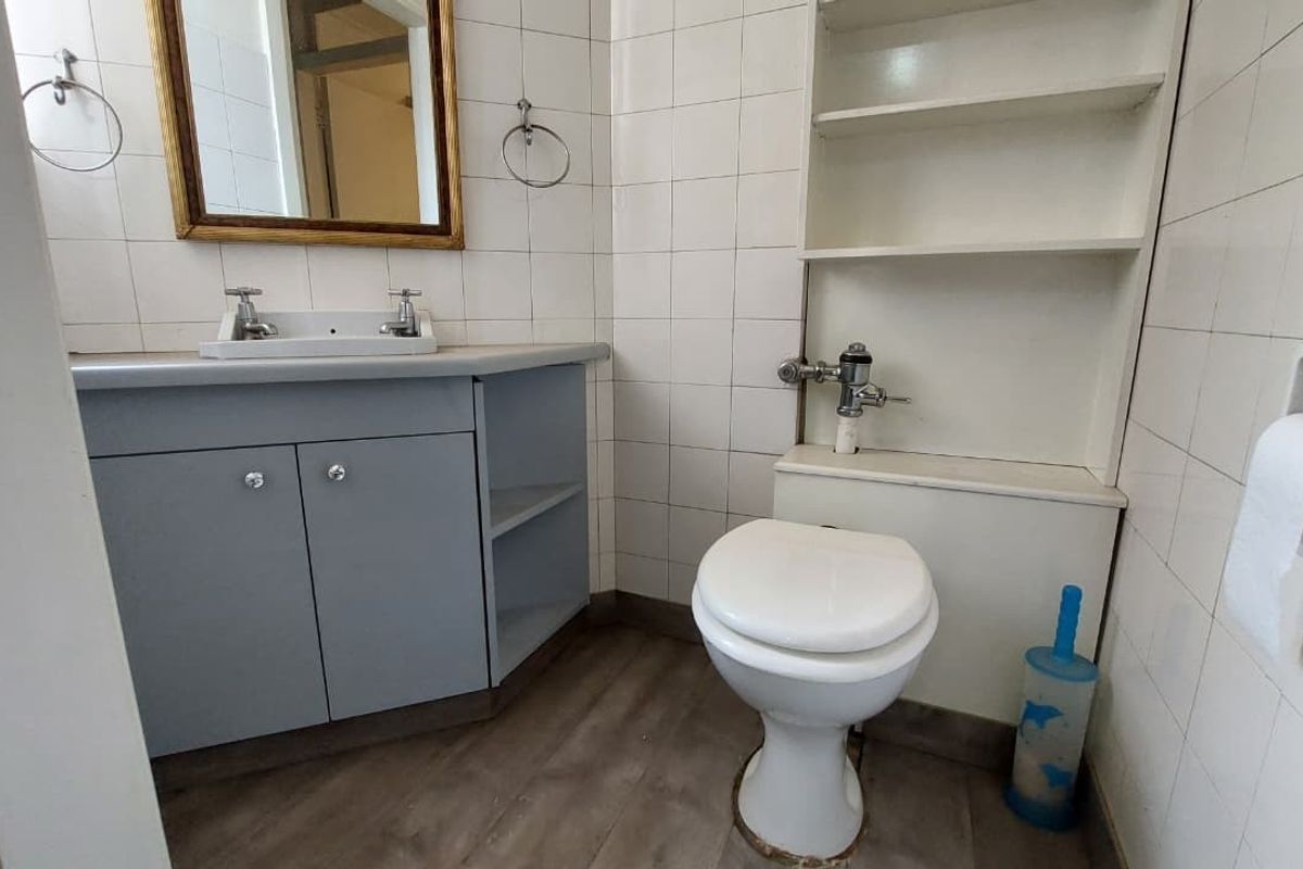 A functional bathroom featuring a vanity unit with basin, toilet, and built-in shelving, finished with tiled walls and wood-look flooring.