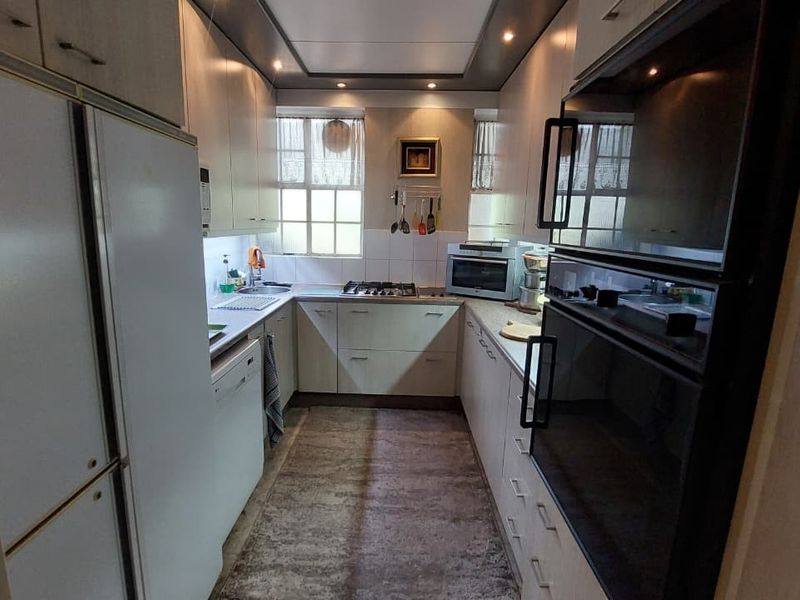 A functional galley-style kitchen featuring built-in cabinetry, integrated oven, gas hob, and stainless steel sink with ample storage space.