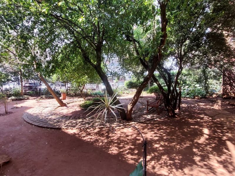 A shaded garden area featuring mature trees, a paved circular pathway, and secure perimeter fencing.