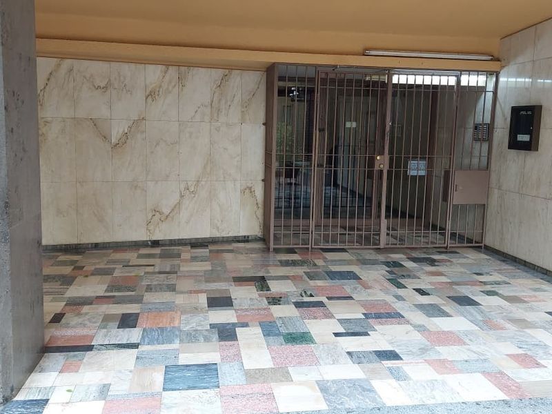 A secure apartment building entrance featuring marble wall cladding, mosaic marble flooring, and a metal security gate with an integrated intercom system.